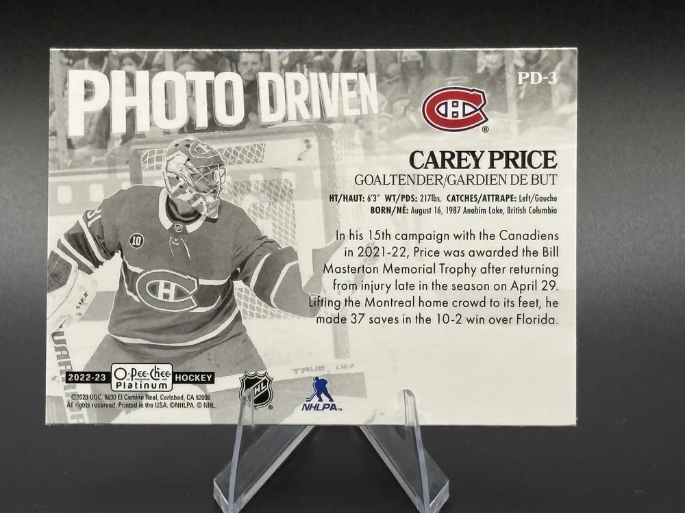 Back of a 2022-23 O-Pee-Chee Platinum Photo Driven Carey Price card in a clear stand, with the stand's arms in front of the bottom edge